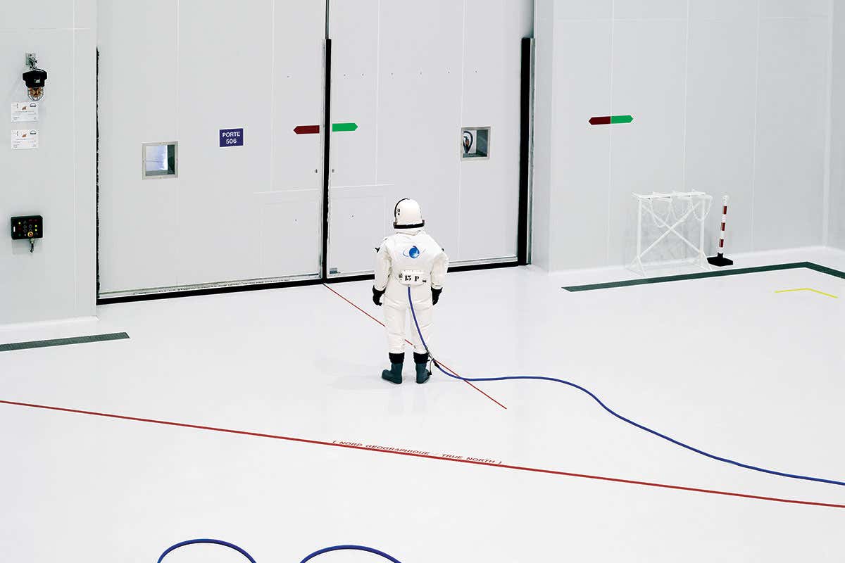 Person in spacesuit standing in front of a large door in a large white industrial room