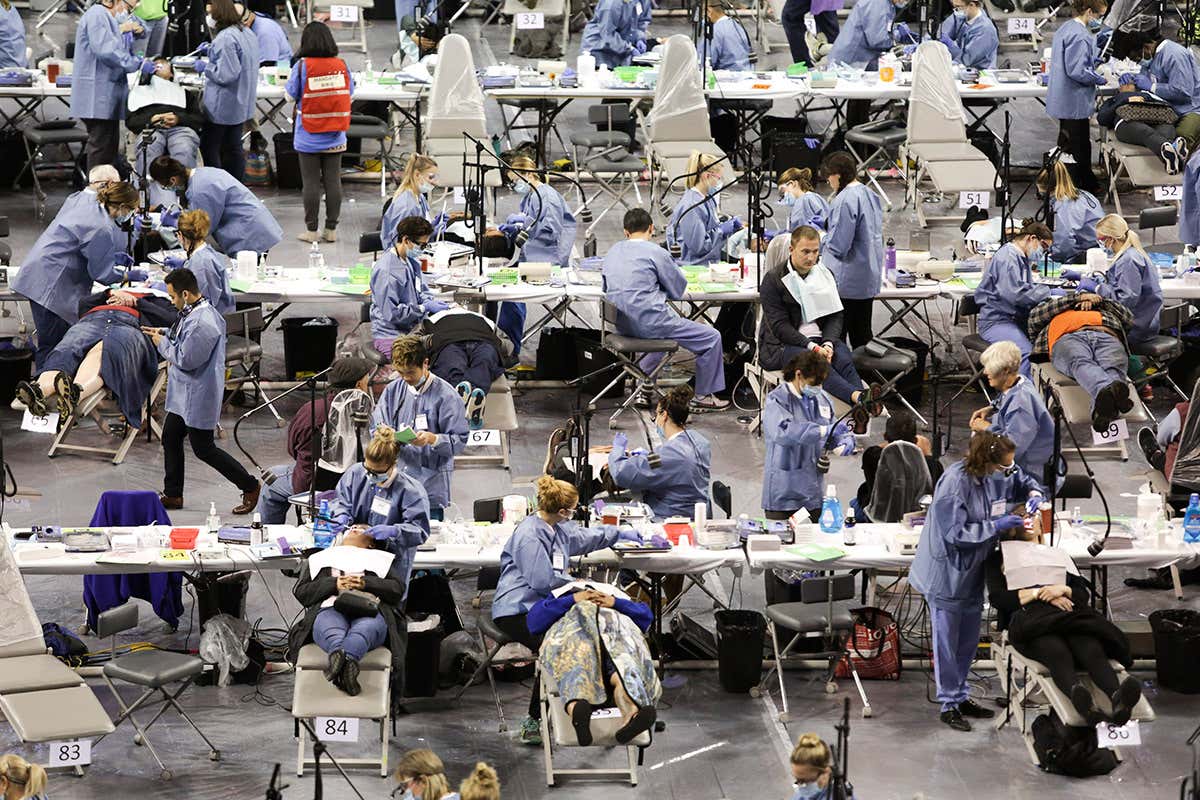 A chaotic looking hall with rows of tables holding medical instruments and medical professionals in scrubs attending to people