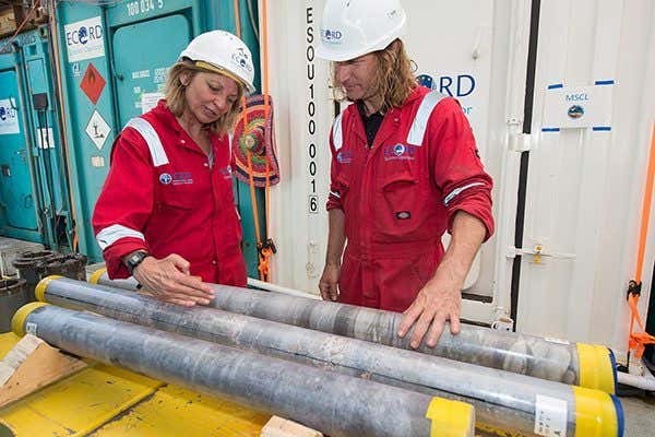 Joanna Morgan and Sean Gulick stand neck to some rock samples wearing hard hats