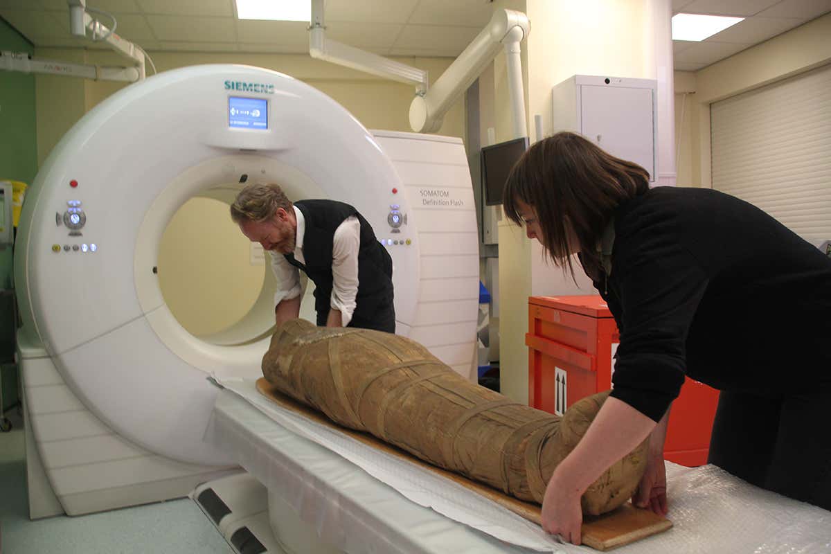 A wrapped mummy going into a CT scanner