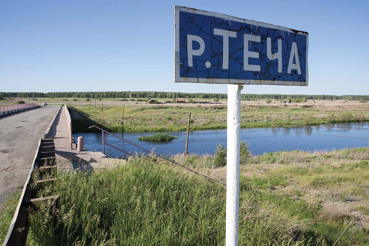 Road sign with Cyrillic script with river and grassland beyond