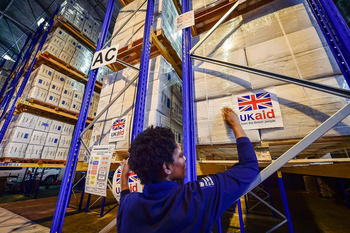 A worker in a warehouse stacks boxes marked with a union jack flag and 