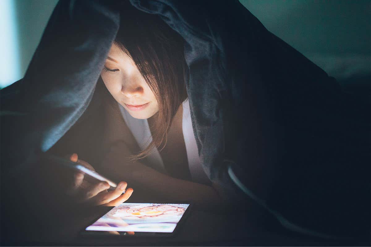 Woman reading a phone and a tablet under a blanket