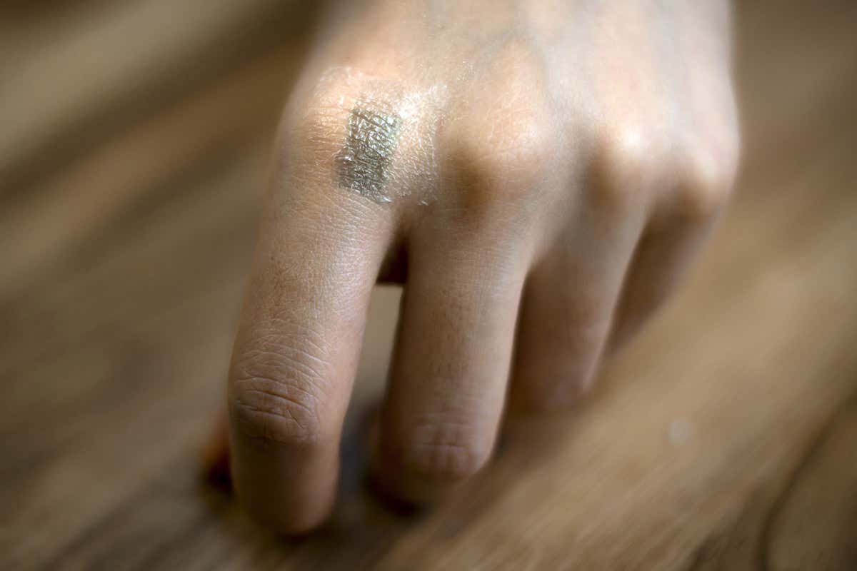 A hand with a stretchy transitor tattooed on the knuckle of first finger