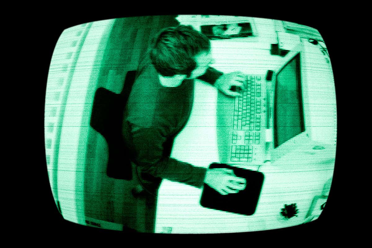 A security camera image of a worker using their computer by a desk