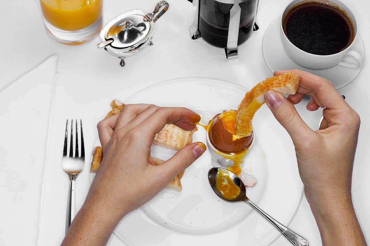 A breakfast table with coffee, orange juice, boiled egg and toast
