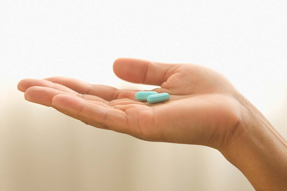 A hand holding two blue pills
