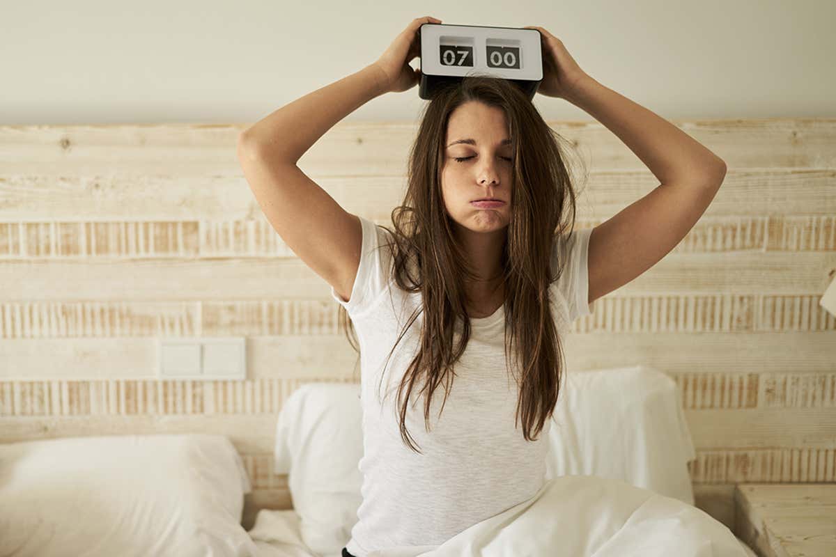 Tired woman holding alarm clock on head