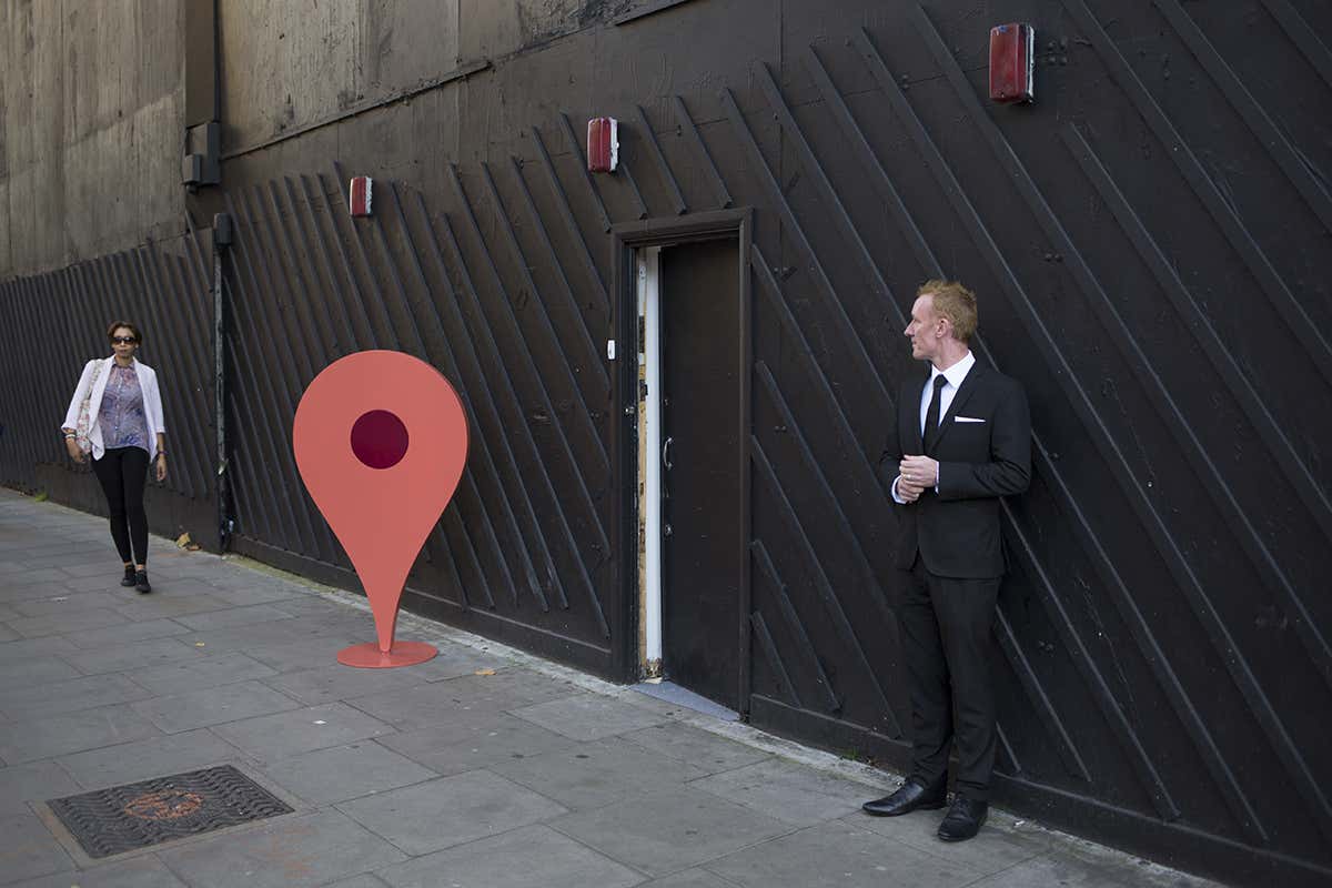 Boarded up street frontage with a physical recreation of a Google Maps pin in front of it