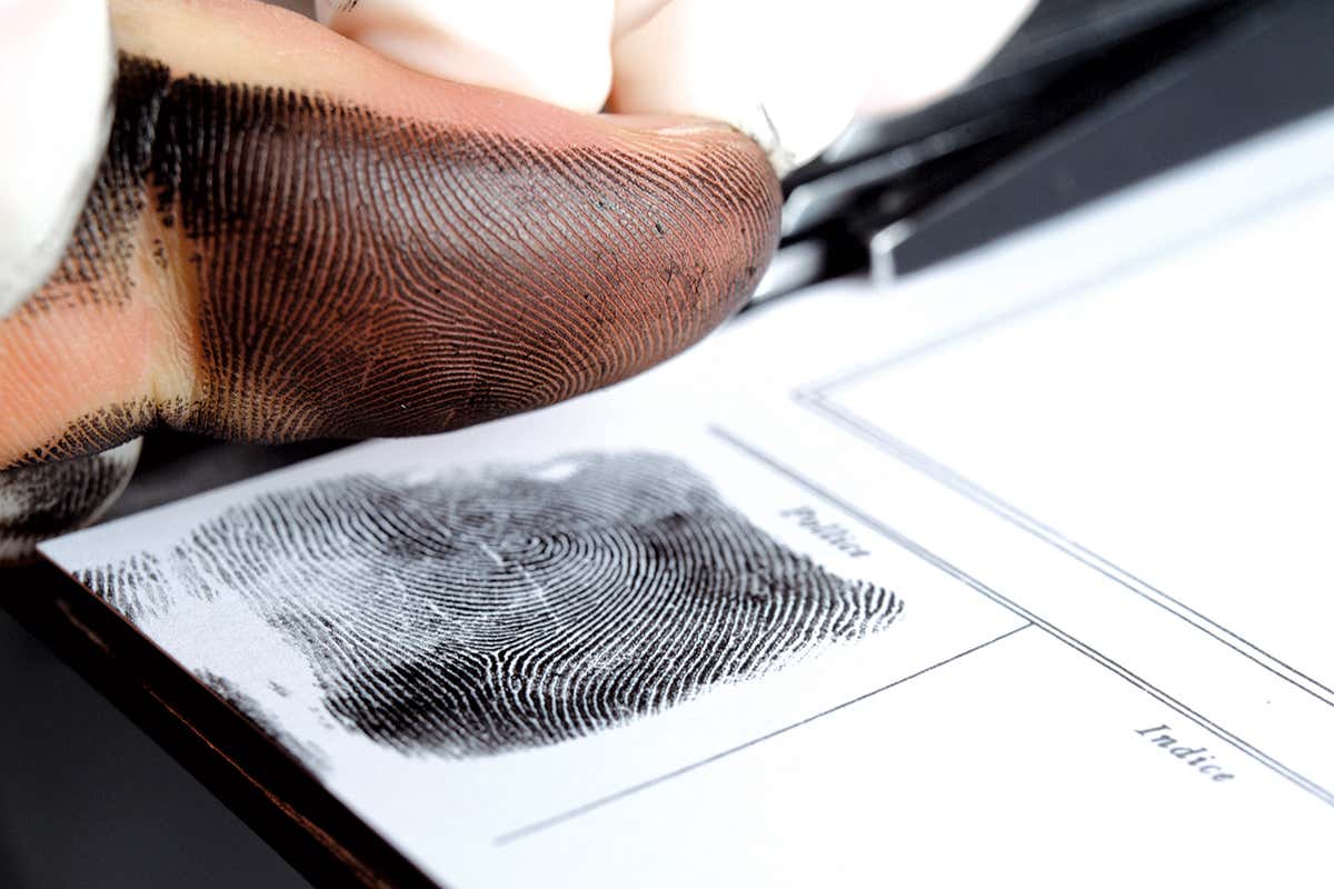 Hand guides another hand so that inky fingerprints can be captured