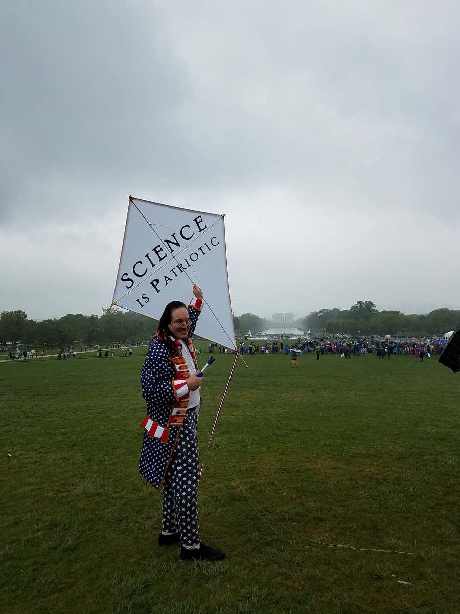A man dressed as Ben Franklin flying a kite in the rain, with the Lincoln Memorial in the background