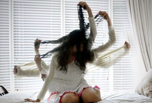 Woman kneeling on a bed pulling her hair in several directions