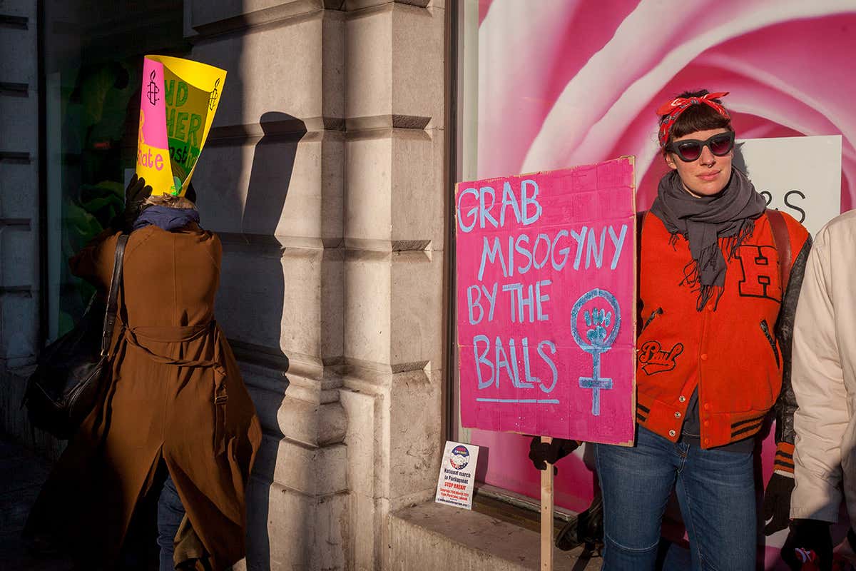 A woman at a protest standing in front of a large picture of a rose holding a sign that says 