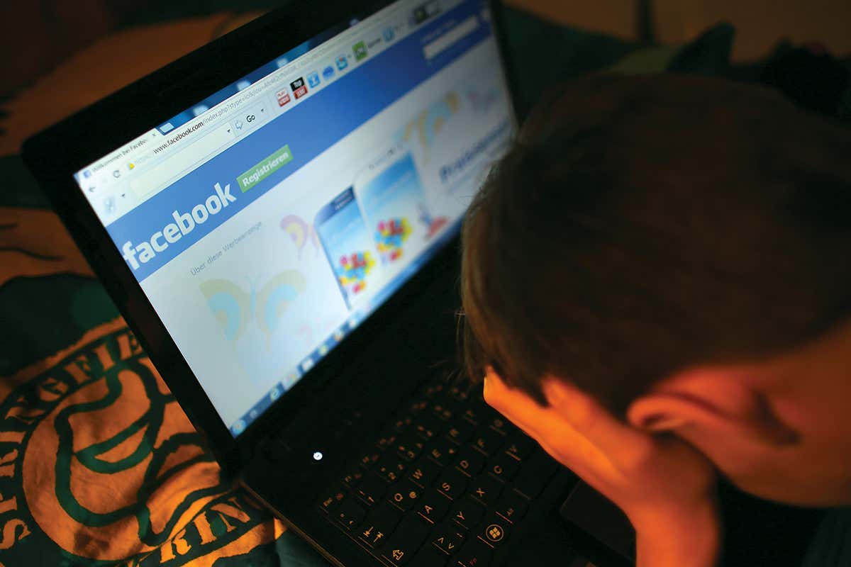 A person with their head in their hands over a laptop displaying the Facebook login page
