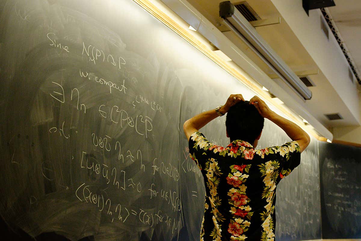 Person throws up at hands standing at blackboard covered in equations