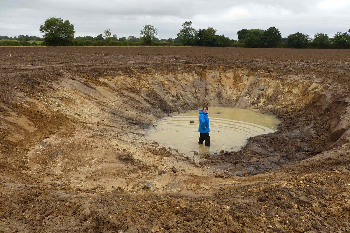 A woman standing in a muddy ditch in farmland