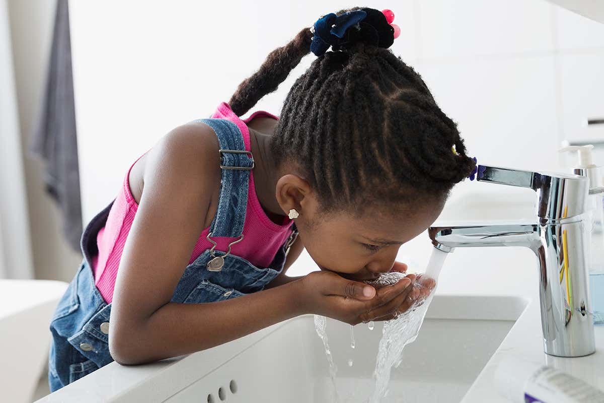 A young girl drinking water from a tap
