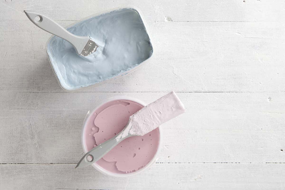 Two open tins of paint side by side on teh floor – one is blue, the other is pink