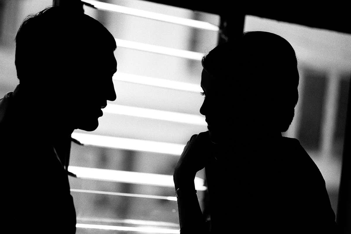 The silhouettes of two people sat talking over a table
