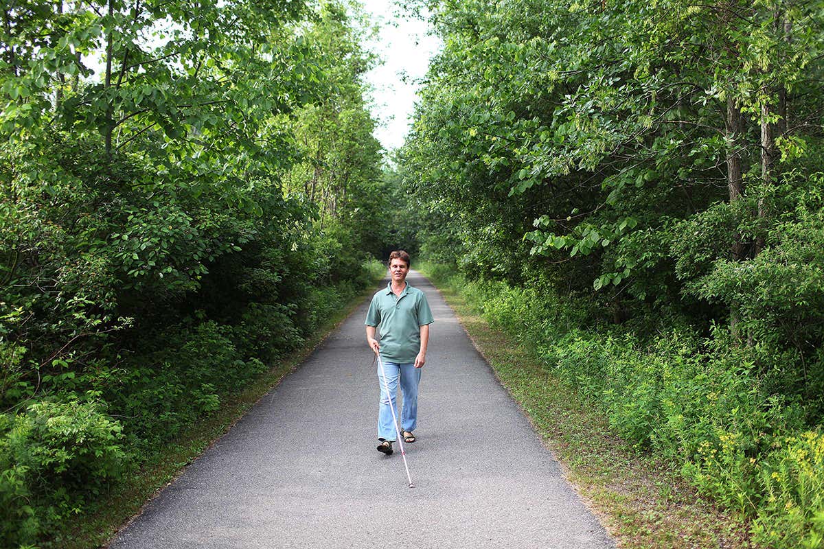 Daniel Kish walks down narrow path flanked by trees