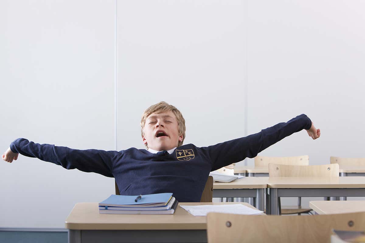 A teenager at a school desk stretching back and yawning