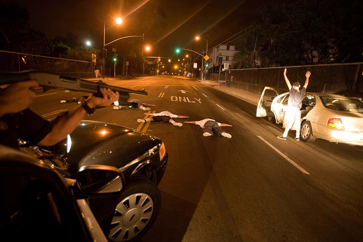 People lie on the ground as a police officer points a gun