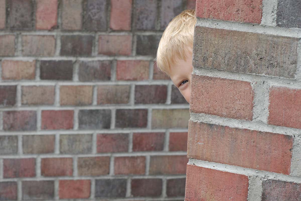 Boy peering round corner of brick wall