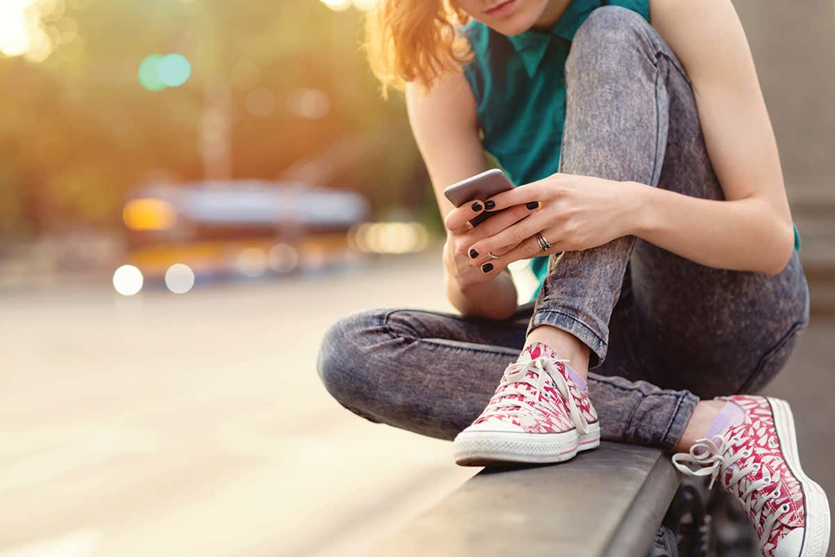 A teen sat on a wall outside typing on a cellphone