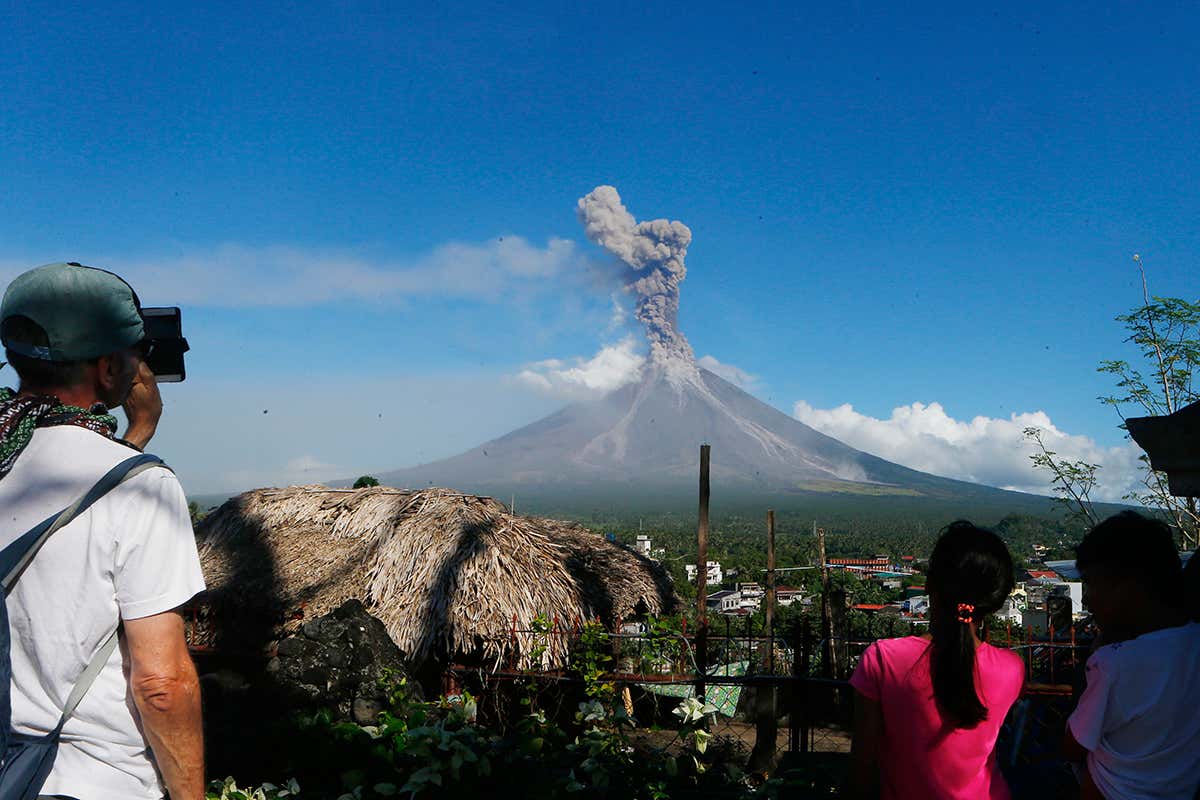 Onlookers watch from a safe distance as the volcano belches plumes of ash into the air