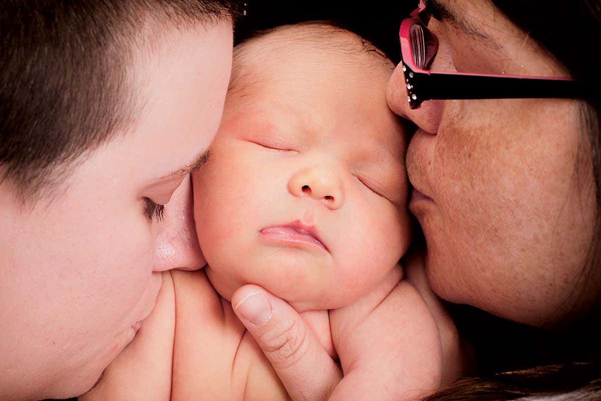 A baby being kissed on either cheek by two women