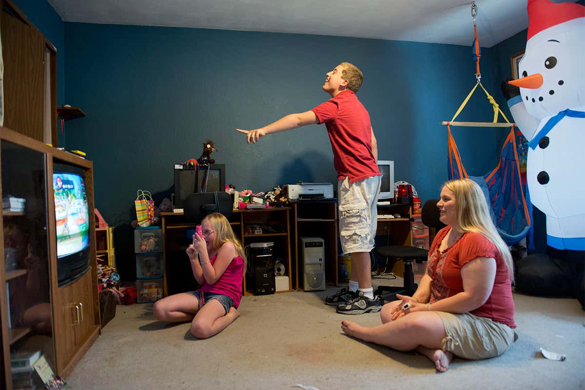 Two children sat playing video games at home with their mother