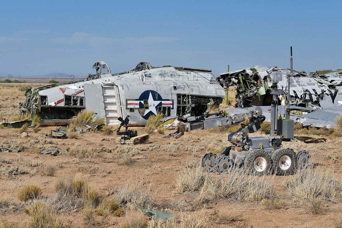 A bomb squad robot in a field with a plane wreakage
