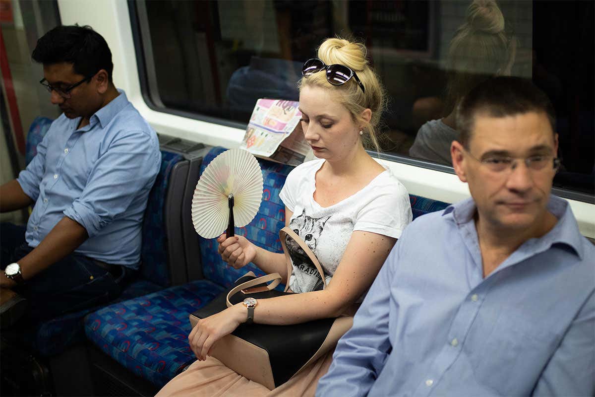 A girl on the underground system uses a fan to attempt to keep cool