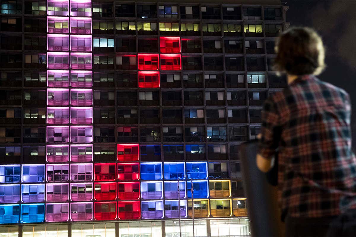 A person looks at a building lit up like a game of Tetris