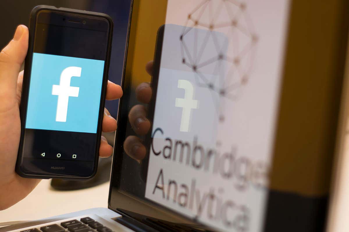 A picture of Facebook on a phone with Cambridge Analytica in the background