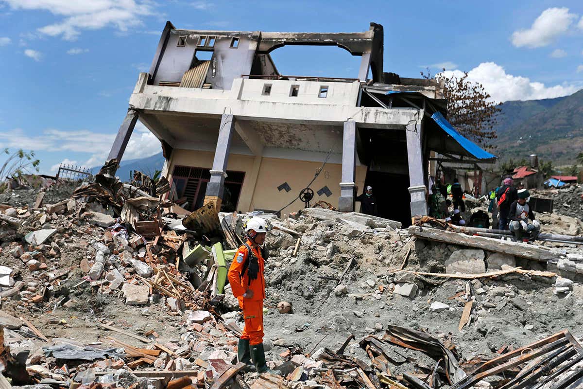 A rescue worker stands neat a collapsed house