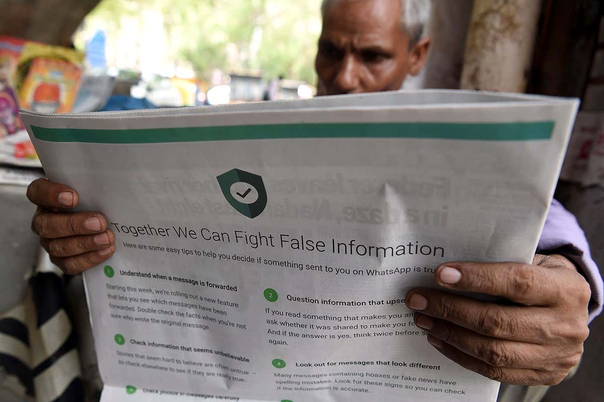 an Indian newspaper vendor reading a newspaper with a full back page advertisement from WhatsApp intended to counter fake information, in New Delhi on July 10, 2018