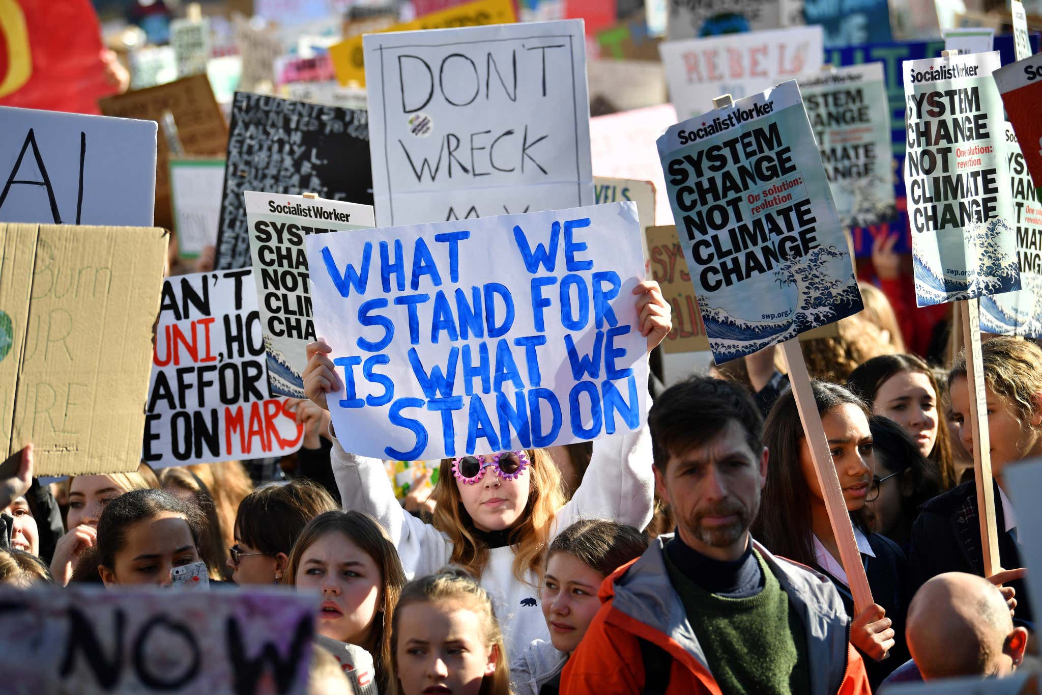 Schoolchildren holding climate protest signs including one saying 'what we stand for is what we stand on'