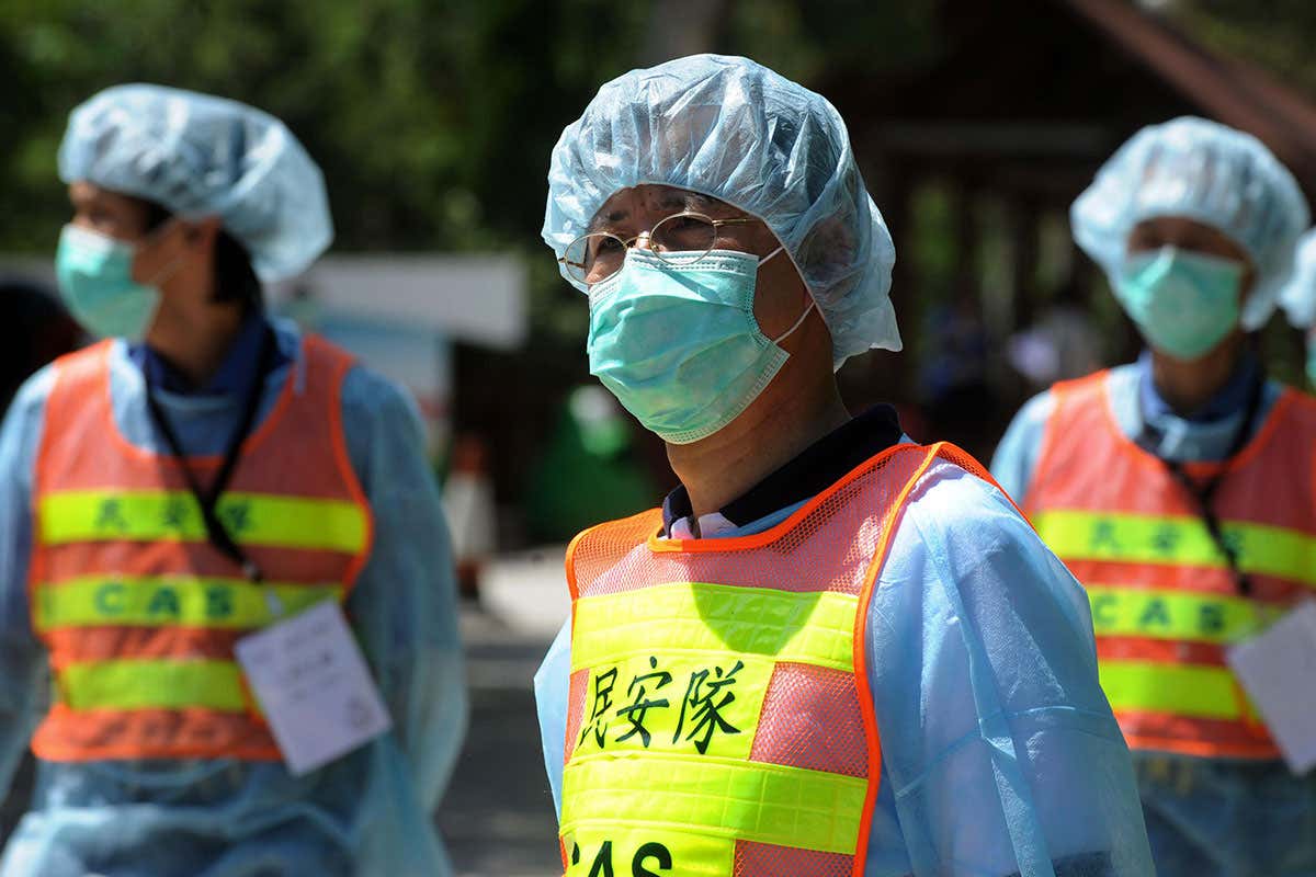 Masked workers wait at the entrance after a group of people formerly under quarantine from swine flu leave a holiday centre turned into quarantine center in Hong Kong on May 7, 2009. Twenty-eight people were released from the centre after seven days of quarantine as they had arrived in Shanghai on a flight with an infected Mexican who had swine flu