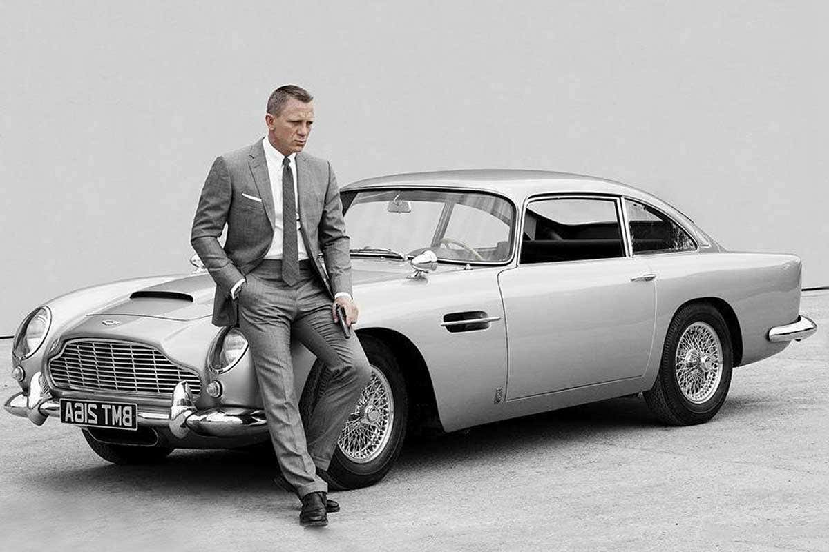 Daniel Craig as James Bond, leaning on an Aston Martin