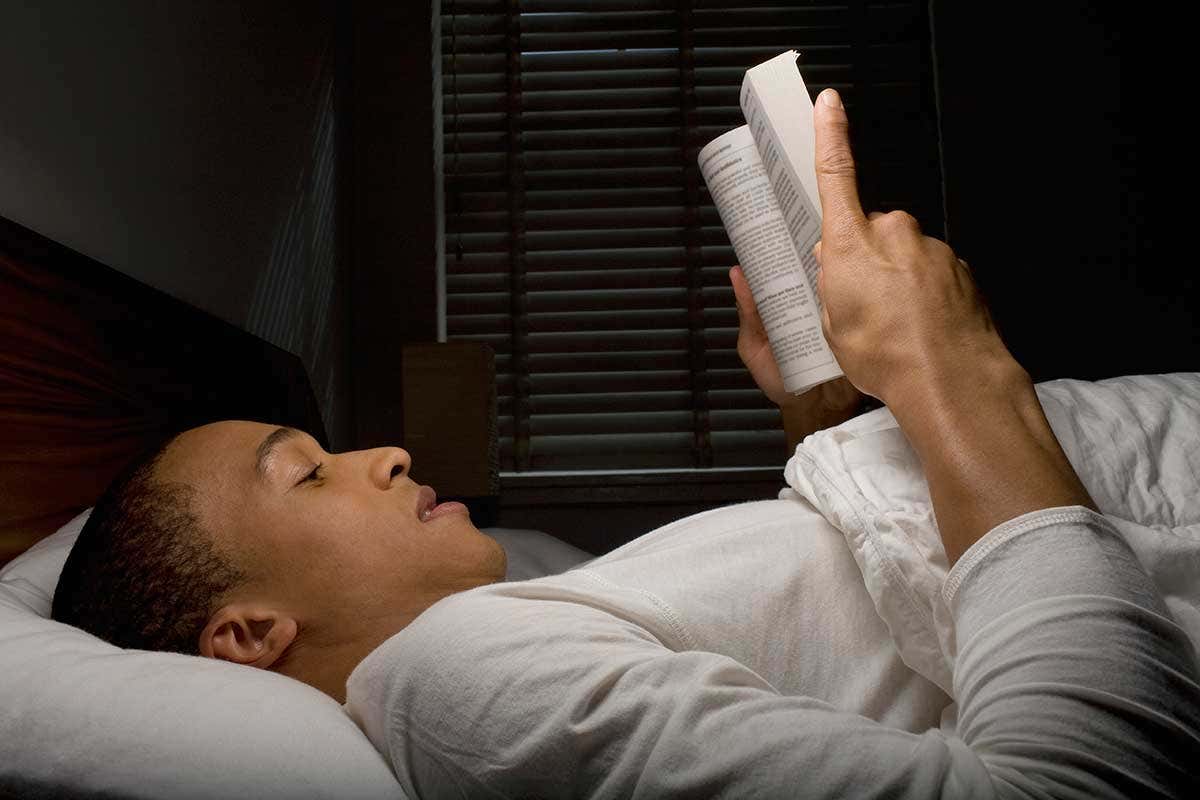 a man lying on a bed reading a book