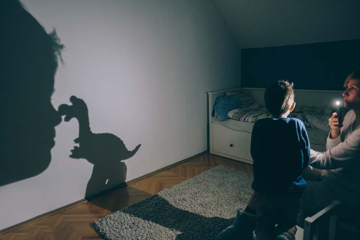 child being read a bedtime story with a dinosaur shadow on the wall