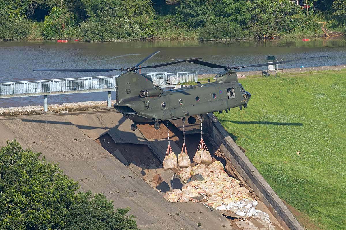 An RAF helicopter drops bags of aggregate to shore up the dam and divert water