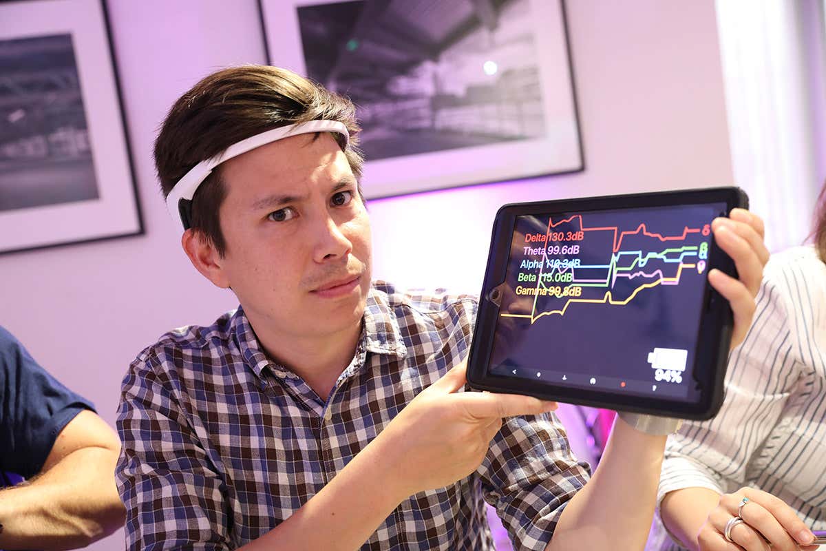 Reporter wearing EEG headset with a tablet display showing brain signals.