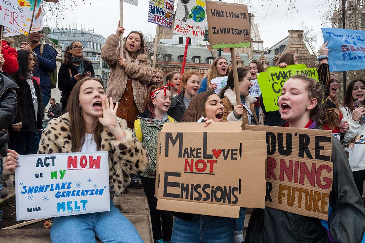 School students campaigning against climate change gather outside Parliament, London with colourful home made banner