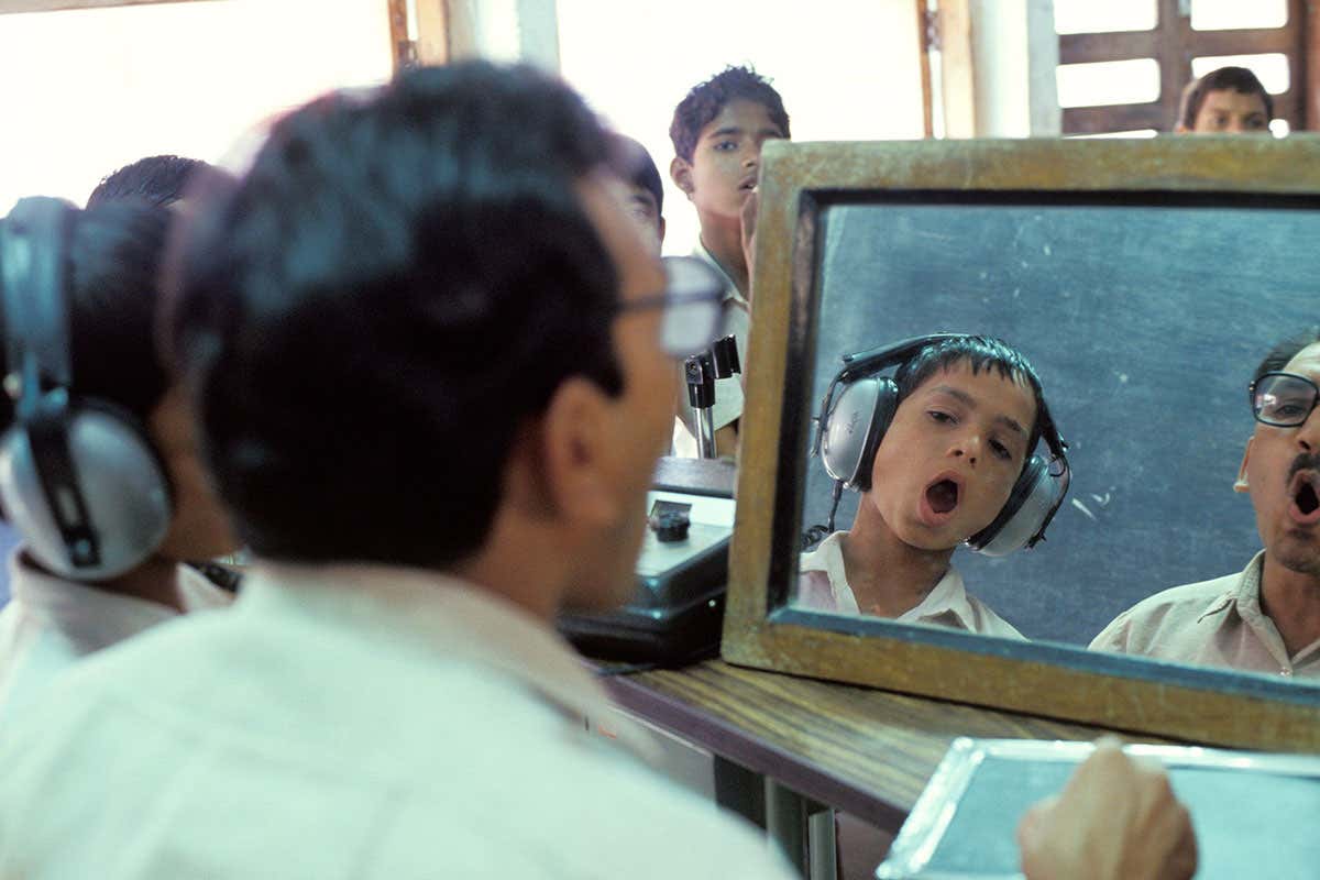 Teacher educates through sight, touch to feel vibration, and very loud sounds for the hearing impaired, at a deaf and dumb school