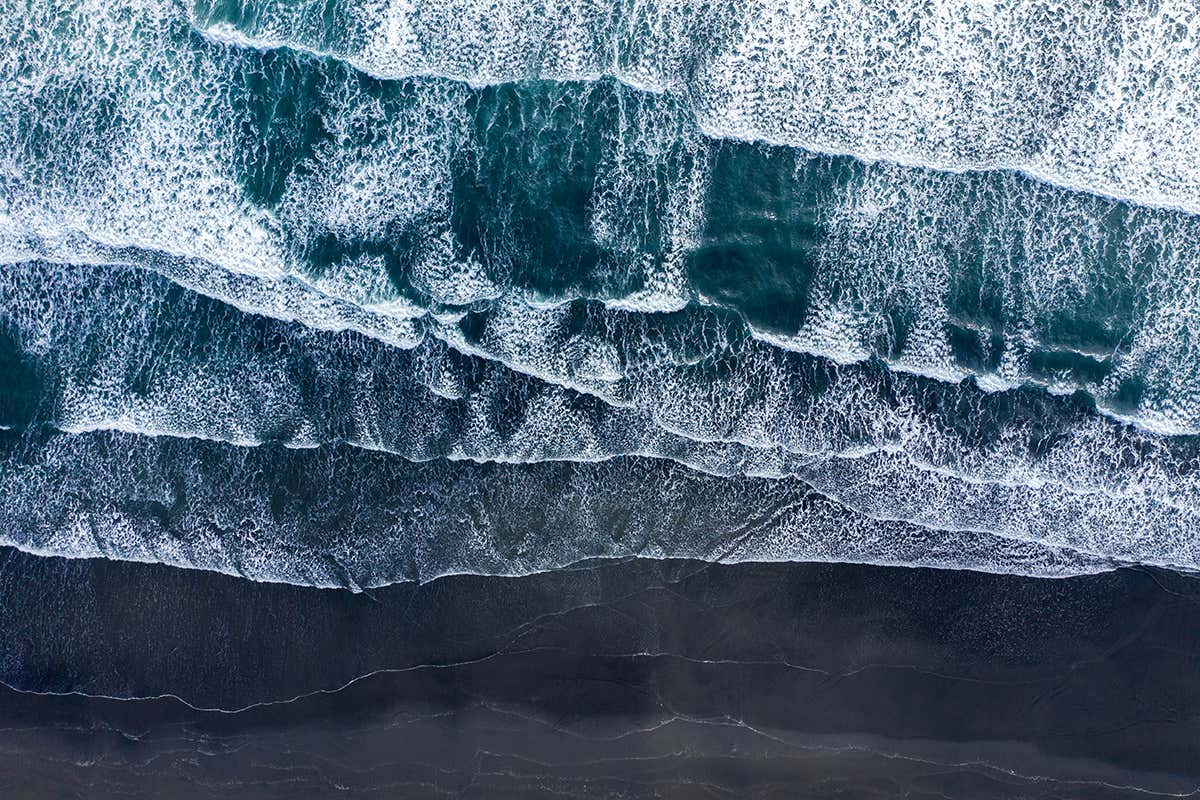 Aerial drone view of Atlantic ocean waves washing black basaltic sand beach, Iceland