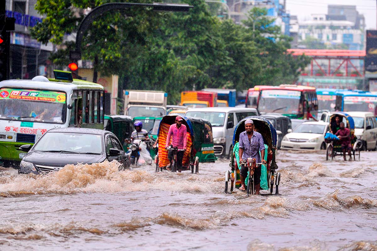Bangladeshi rickshaw pullers make their way through heavy rainfall at a water-logged street during the monsoon season in
