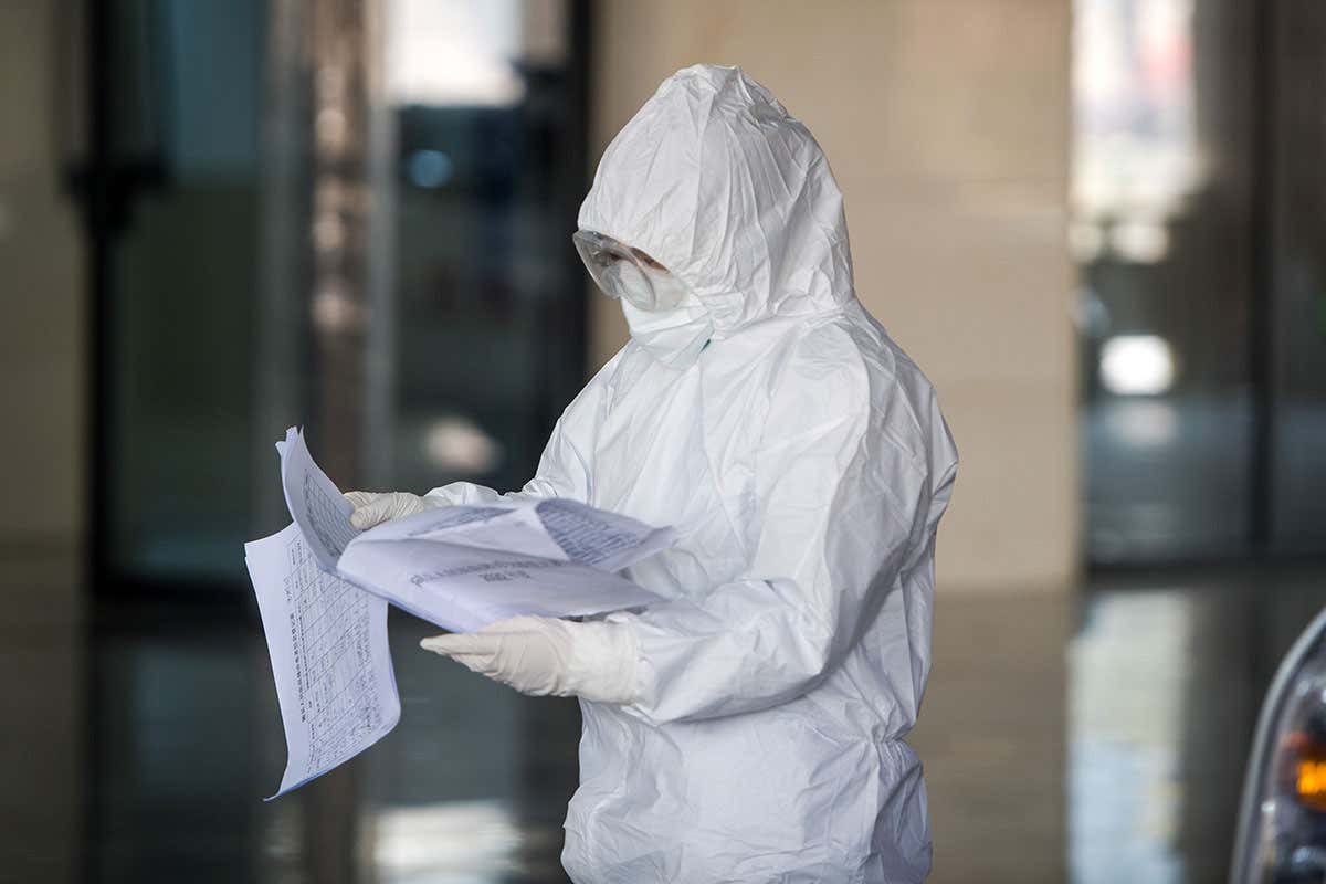 A person in a hazmat suit reads a piece of paper