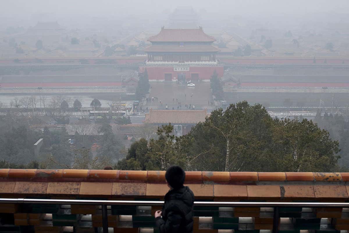 A man is looking at the north gate of the Forbidden City lost in the smog of pollution from the top of the Coal Hill, Beijing